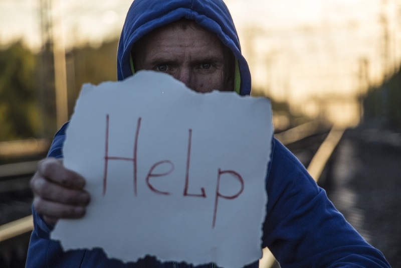 man in hoodie holding a hand written help sign